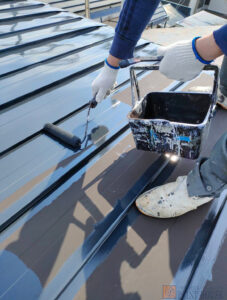 函館市での屋根塗装の施工風景。職人がローラーで丁寧に塗り替えている様子。